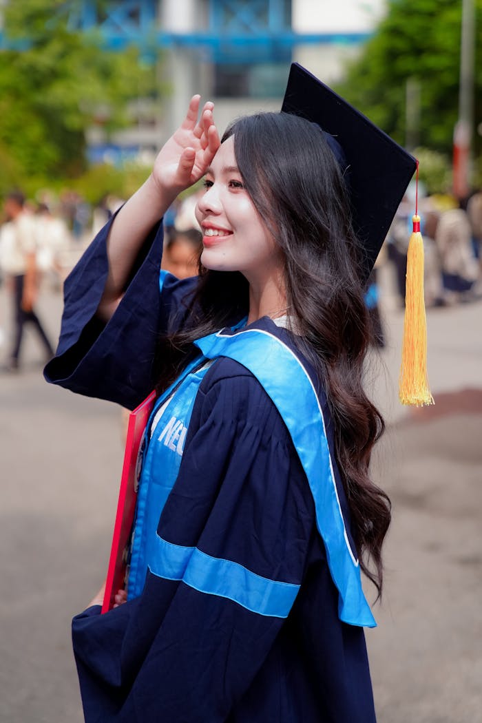 Smiling young woman in graduation gown and cap celebrating outdoors.